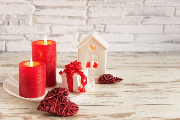 Composición romántica para el día de San Valentín con velas y corazones en la mesa de madera sobre pared de ladrillo blanco.