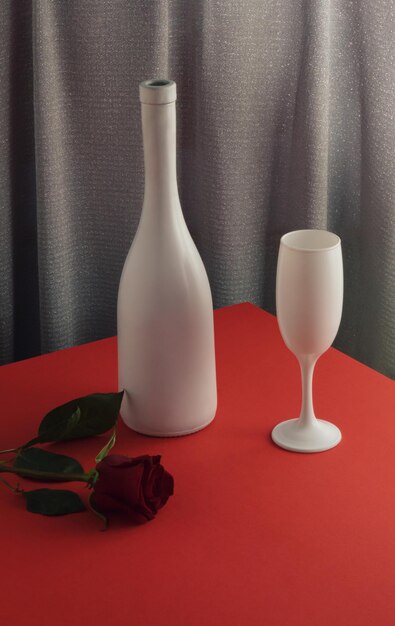Composición romántica mínima de San Valentín con copa de botella de vino blanco y flor de rosa en la mesa