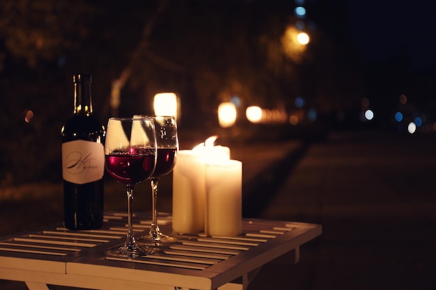 Composición romántica con velas encendidas y vino en la mesa al aire libre por la noche