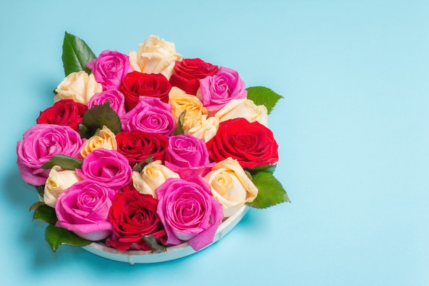 Composición de rosas frescas multicolores sobre soporte de cerámica. El concepto festivo para bodas, cumpleaños, 8 de marzo, día de la madre o San Valentín. Tarjeta de felicitación, endecha plana, fondo azul mate