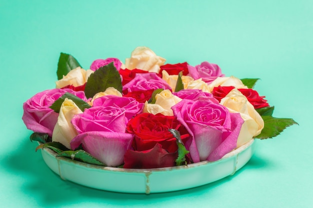 Composición de rosas frescas multicolores sobre soporte de cerámica. El concepto festivo para bodas, cumpleaños, 8 de marzo, día de la madre o San Valentín. Tarjeta de felicitación, endecha plana, fondo turquesa mate