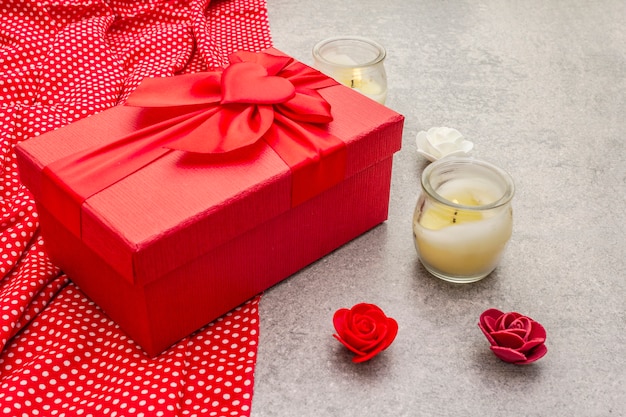 Composición de San Valentín con caja de regalo roja, tela punteada, velas y rosas.