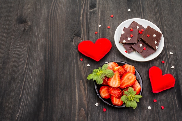 Composición de San Valentín con chocolate, fresas frescas maduras y corazones rojos textiles