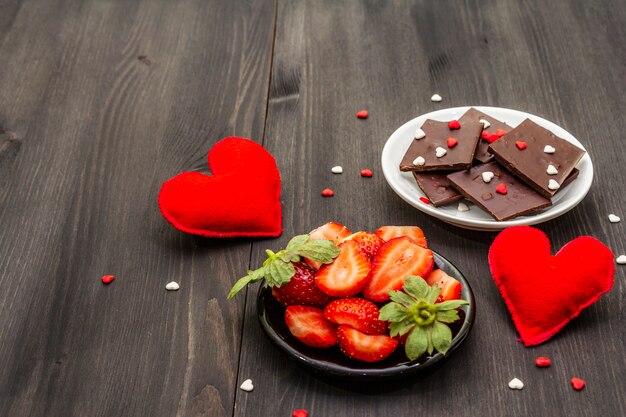 Composición de San Valentín con chocolate, fresas frescas maduras y corazones rojos textiles