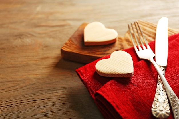 Composición de servilleta de tenedor y corazones decorativos en tabla de cortar sobre fondo de mesa de madera