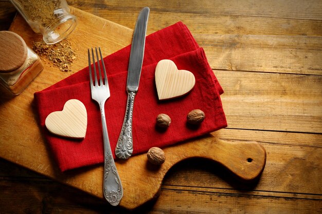 Composición de servilleta de tenedor y corazones decorativos en tabla de cortar sobre fondo de mesa de madera