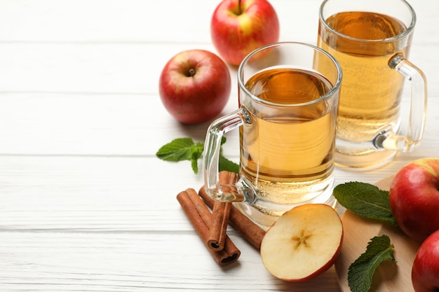 Composición con sidra, canela y manzanas en madera blanca