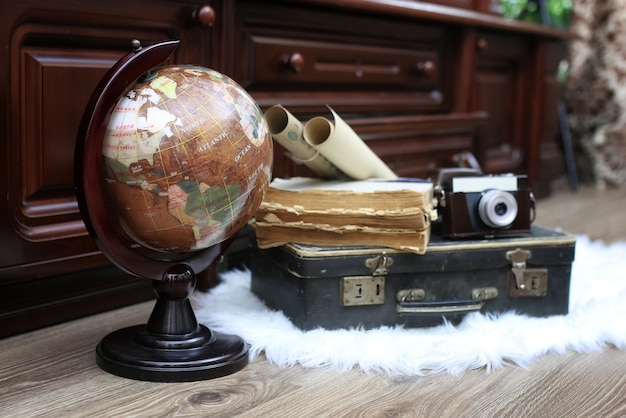 Composición sobre un piso de madera globo vintage con maleta de cuero antiguo con objetos para viajar