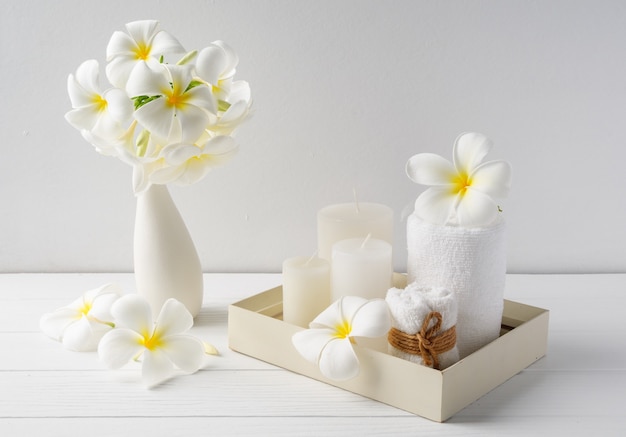 Composición de spa hermosas flores de plumeria, velas blancas y toallas en bandeja de madera en la superficie interior de la sala de mesa de madera blanca