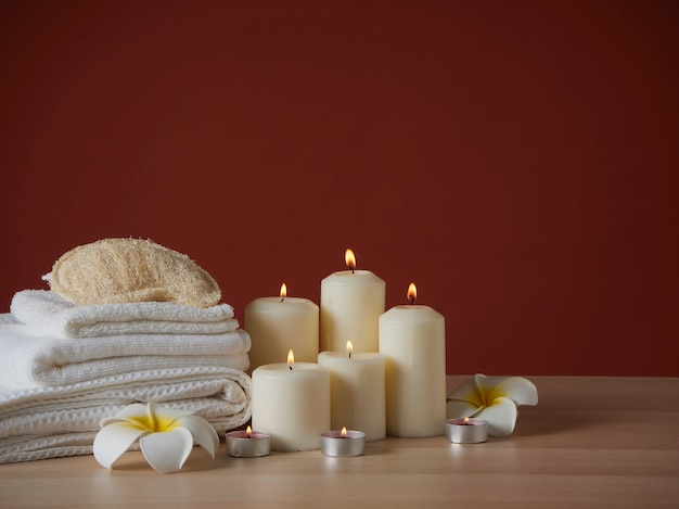 Composición de spa con velas aromáticas encendidas y flores de plumeria en mesa de madera