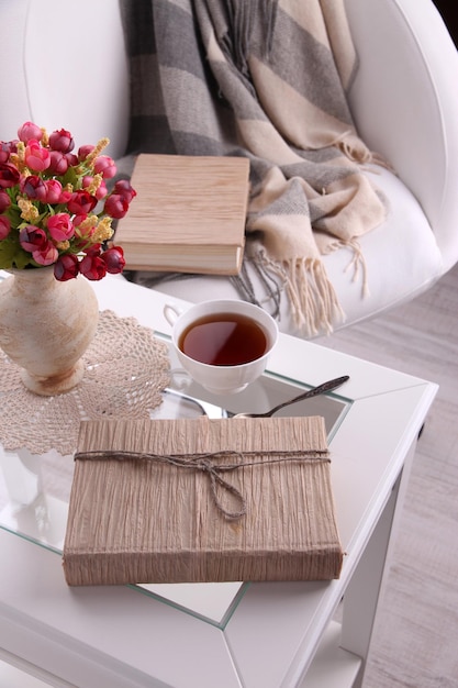 Composición con taza de bebida caliente y galletas en mesa de madera cerca de sillón