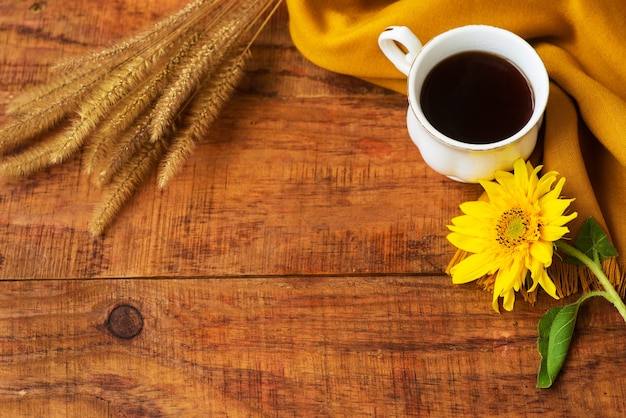 Composición de la taza de té de otoño, pañuelo amarillo, espiguillas de trigo y flor de girasol sobre un fondo de madera