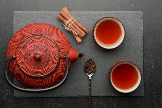 Composición de té con tazas de té de cerámica y tetera de hierro rojo.