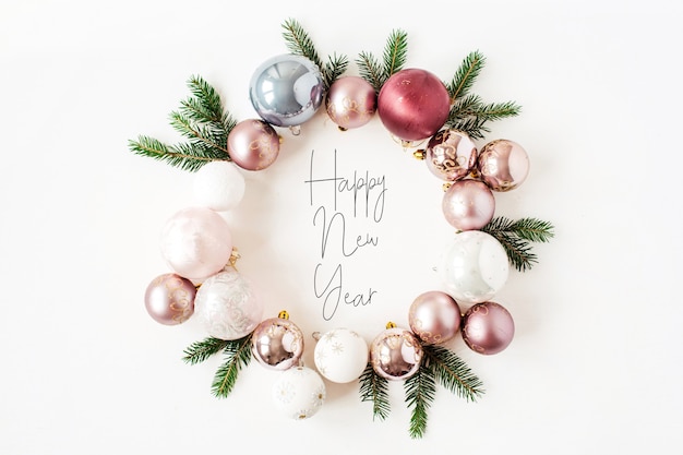 Composición de vacaciones de Navidad año nuevo. Cita "Feliz año nuevo" en corona de marco con adornos navideños, bolas y ramas de abeto en blanco