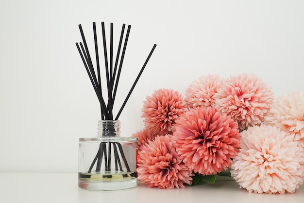 Composición con varitas de incienso aceite esencial en un jarrón de cristal y flores artificiales de rizo rosa en el interior de una habitación blanca Fondo blanco Muchas flores y varitas aromáticas