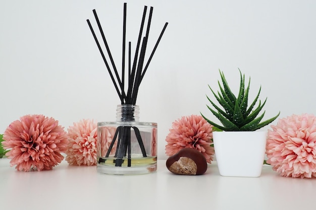 Composición de varitas de incienso de flores artificiales rosadas en un jarrón de vidrio con aceite esencial Bodegón sobre una mesa blanca Flor de aloe en una maceta blanca Diseño de interiores de decoración de habitaciones y apartamentos