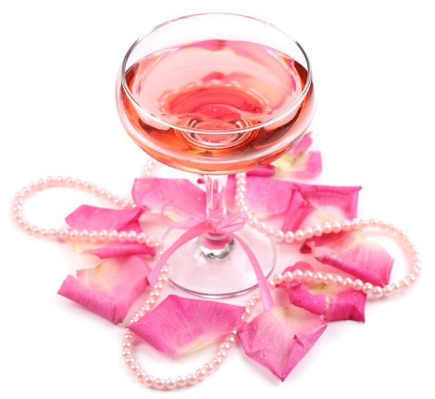 Composición con vino espumoso rosa en copa y pétalos de rosa aislados en blanco