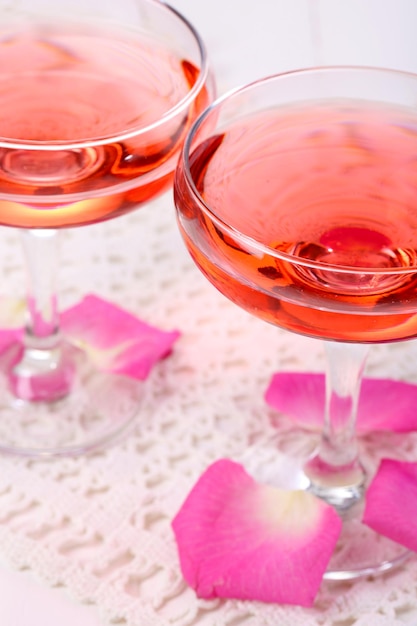 Composición con vino espumoso rosa en copas y pétalos de rosa aislados en blanco