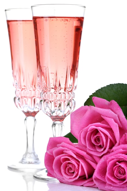 Composición con vino espumoso rosa en copas y rosas rosadas aisladas en blanco