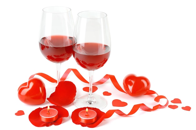 Composición con vino tinto en copas, rosas rojas, cinta y corazones decorativos aislados en blanco