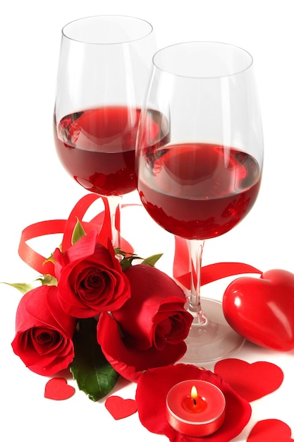 Composición con vino tinto en copas, rosas rojas, cinta y corazones decorativos sobre fondo claro