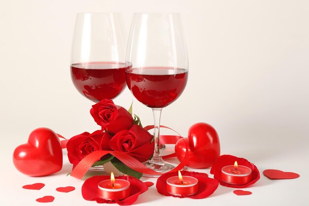Composición con vino tinto en copas, rosas rojas, cinta y corazones decorativos sobre fondo claro
