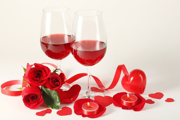 Composición con vino tinto en copas, rosas rojas, cinta y corazones decorativos