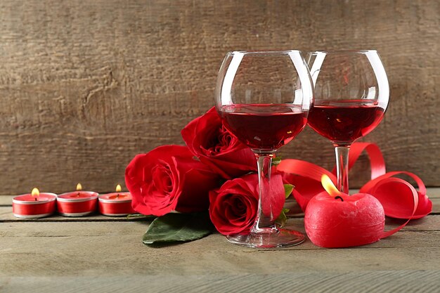 Composición con vino tinto en copas, rosas rojas y corazón decorativo sobre fondo de madera