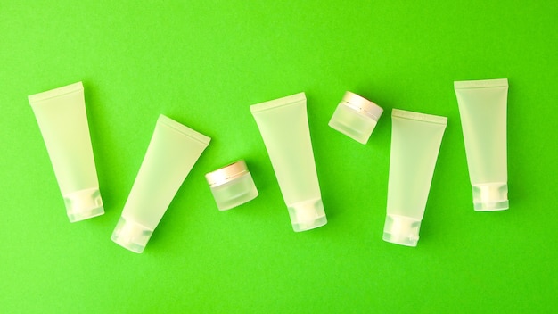 Composición de la vista superior de pequeñas botellas de viaje y frascos para productos cosméticos sobre fondo verde. Concepto de cuidado de la piel facial con espacio de copia para su diseño. Maqueta cosmética