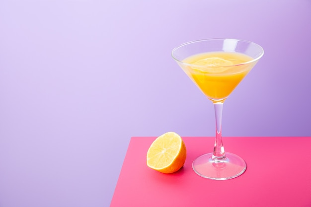 Composición vívida brillante con copa de cóctel de bebida amarilla y limón fresco colocado sobre fondo de colores