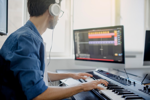 Compositor manos en las teclas del piano en el estudio de grabación. Tecnología de producción musical, el hombre está trabajando en pianino y el teclado de la computadora en el escritorio.