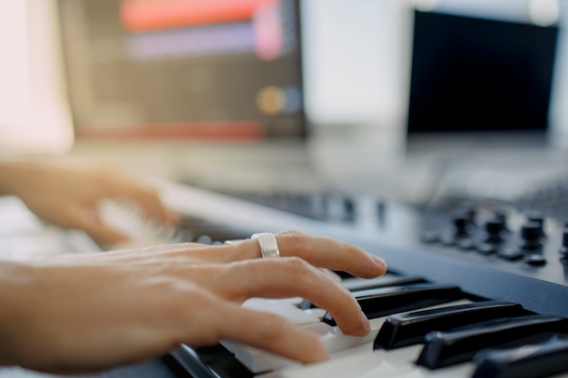 Compositor mãos nas teclas de piano no estúdio de gravação. tecnologia de produção musical, o homem está trabalhando no teclado pianino e computador na mesa. fechar o conceito.