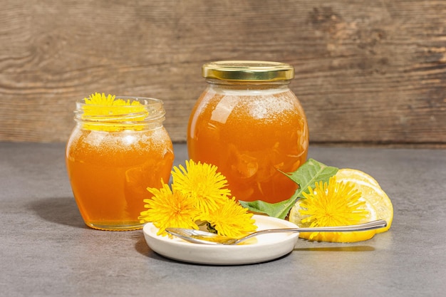 Compota de dente-de-leão ou mel no frasco de vidro com flores frescas de dente-de-leão Sombra escura de luz dura na moda