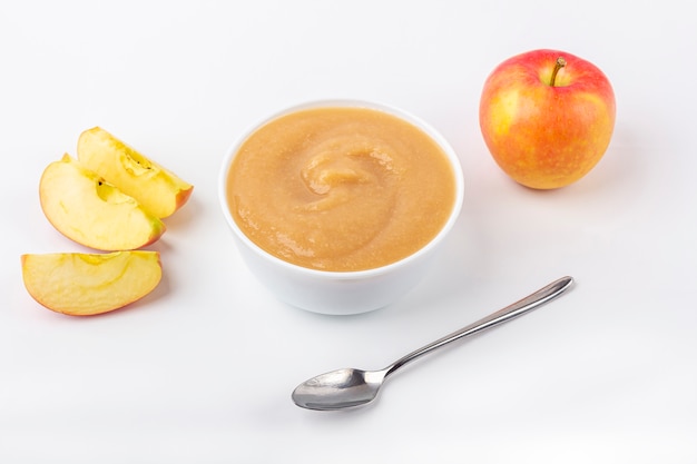 Compota de manzana casera fresca. El concepto de nutrición adecuada y alimentación saludable. Comida orgánica y vegetariana. Tazón blanco con puré de frutas sobre tela y cortar manzanas en la mesa. Comida para bebé.