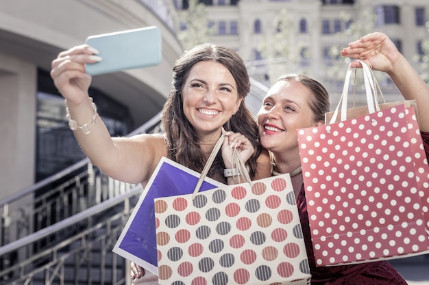 Foto compra bem-sucedida. mulheres felizes e encantadas mostrando suas malas enquanto tiravam fotos juntas