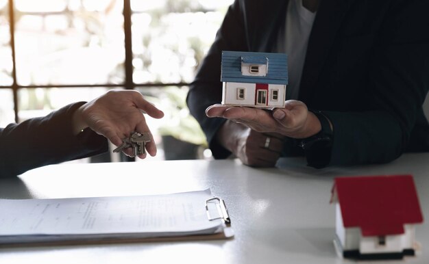 Compra de bienes raíces y concepto de acuerdo Los agentes inmobiliarios acuerdan comprar una casa y dar llaves a los clientes en las oficinas de su agencia