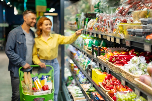 Compra de comestibles pareja joven eligiendo comestibles en el supermercado enfoque selectivo en verduras frescas