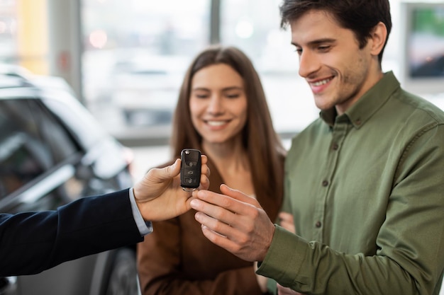 Foto compra de automóveis ou conceito de aluguel feliz jovem casal pegando a chave do carro do vendedor de automóveis em
