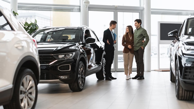 Compra de carro ou aluguel de jovens cônjuges positivos falando com o vendedor sobre a compra de um novo automóvel em