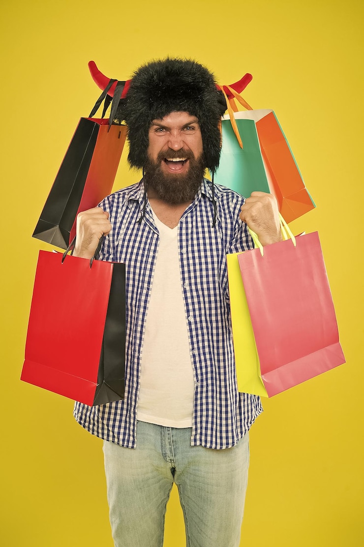 Foto compra maravilhosa homem barbudo sorrindo com compra pessoal hipster feliz com chapéu de chifres de touro segurando sua compra em sacos de papel comprando compra de moda