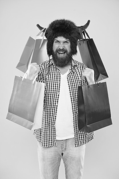 Compra maravilhosa Homem barbudo sorrindo com compra pessoal Hipster feliz com chapéu de chifres de touro segurando sua compra em sacos de papel Comprando compra de moda