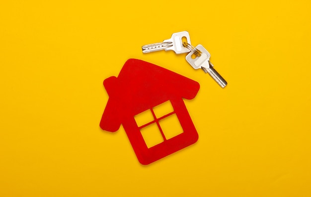 Foto compra ou aluguel de habitação. estatueta de uma casa com chaves em fundo amarelo. vista do topo