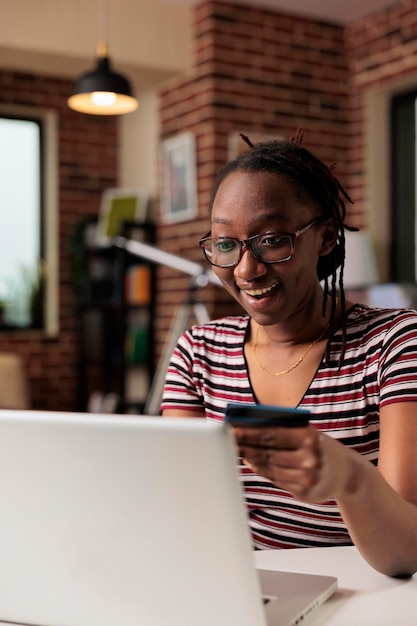 Comprador emocionado con tarjeta de crédito en las manos, compras en línea en casa, pago de compra, compra en la tienda de Internet. Mujer sonriente comprando productos usando laptop, cliente pagando por pedido