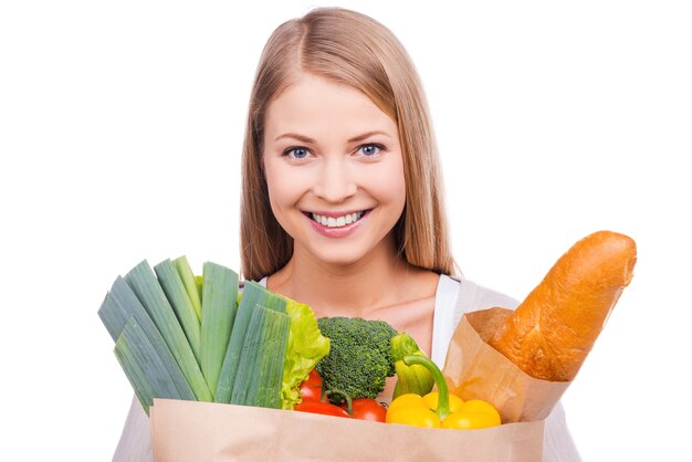 Comprador lindo. mulher jovem e bonita carregando uma sacola de compras cheia de mantimentos e olhando para a câmera em pé contra um fundo branco