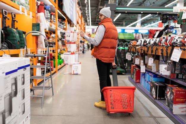 Un comprador masculino en una ferretería con una canasta camina entre las filas de productos