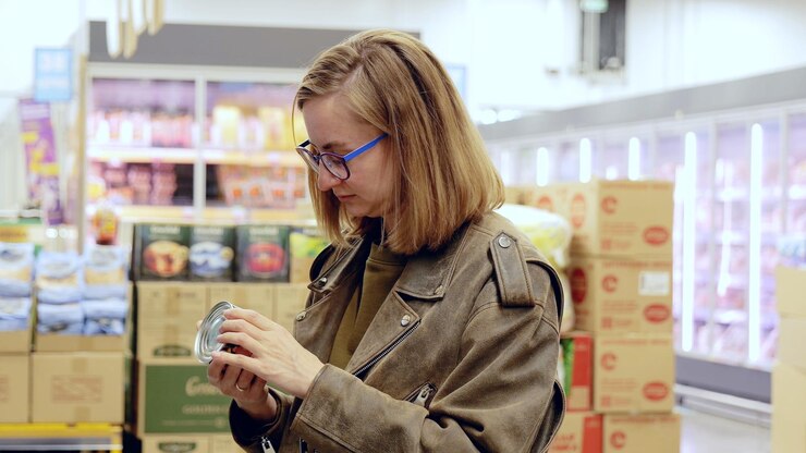 Foto comprador moderno consciente de la salud una mujer joven lee una etiqueta de lata en un pasillo del supermercado considerando