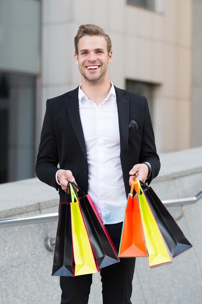 Comprador profesional del estilista del hombre. Mensajero de ropa. El estilista compra ropa de moda al cliente. Concepto de servicio de compras. Centro comercial de traje formal de hombre. El asistente de la tienda ayuda a llevar bolsas de compras.