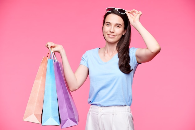 Compradora bonita de camiseta, calça e óculos de sol, isolada na parede rosa