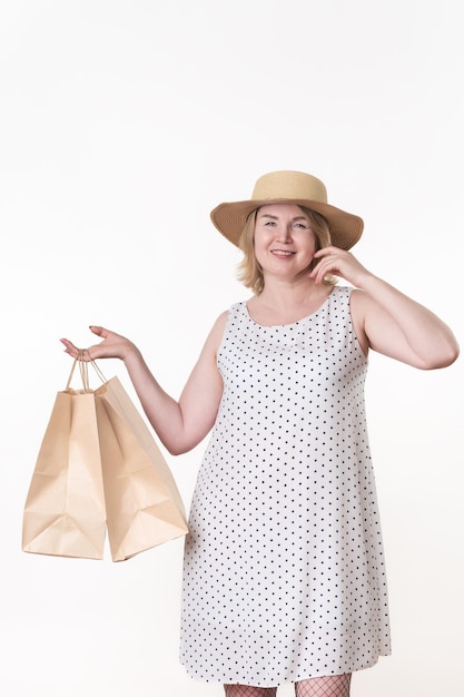 Compradora de 49 anos em vestido branco segurando duas sacolas de papel artesanal em uma mão