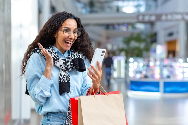 Compradora feliz dentro de la tienda hablando por videollamada con amigas hispanas usando un teléfono inteligente